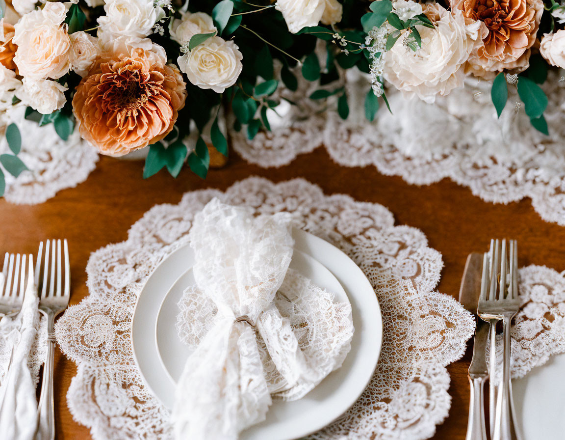 White plates on lace doilies with silver cutlery, peach and white flower centerpiece