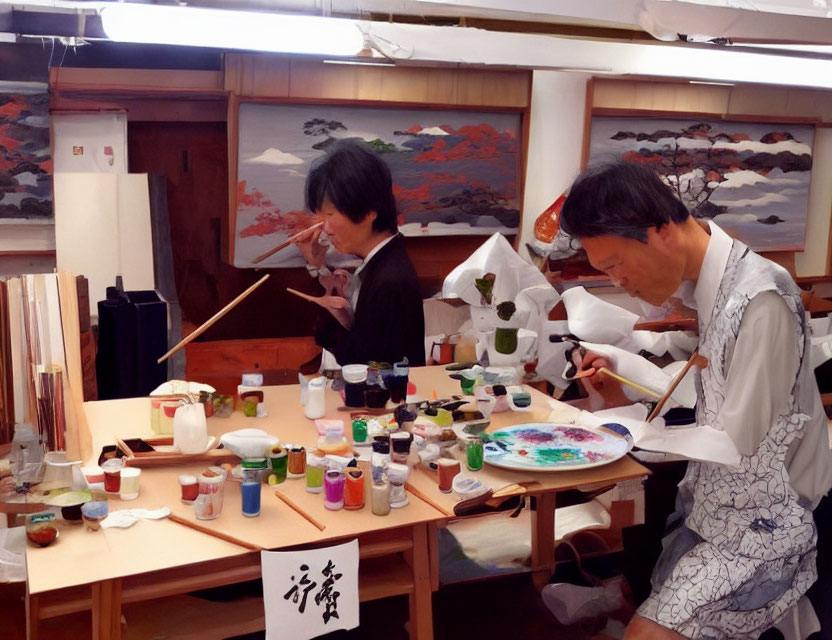 Two individuals painting in a traditional Japanese art class with brushes and colors.