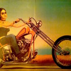 Woman posing on red motorcycle in denim shorts and sleeveless top on hazy yellow background