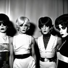 Four women in avant-garde black and white outfits with dramatic makeup and stylish hairdos posing sternly