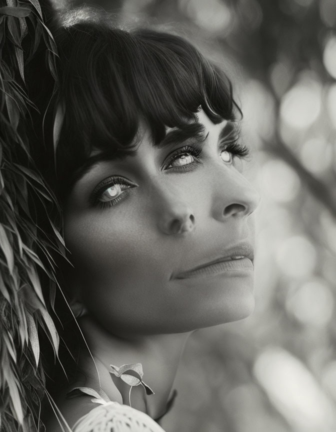 Monochrome portrait of woman with bangs surrounded by leaves and dreamy bokeh.