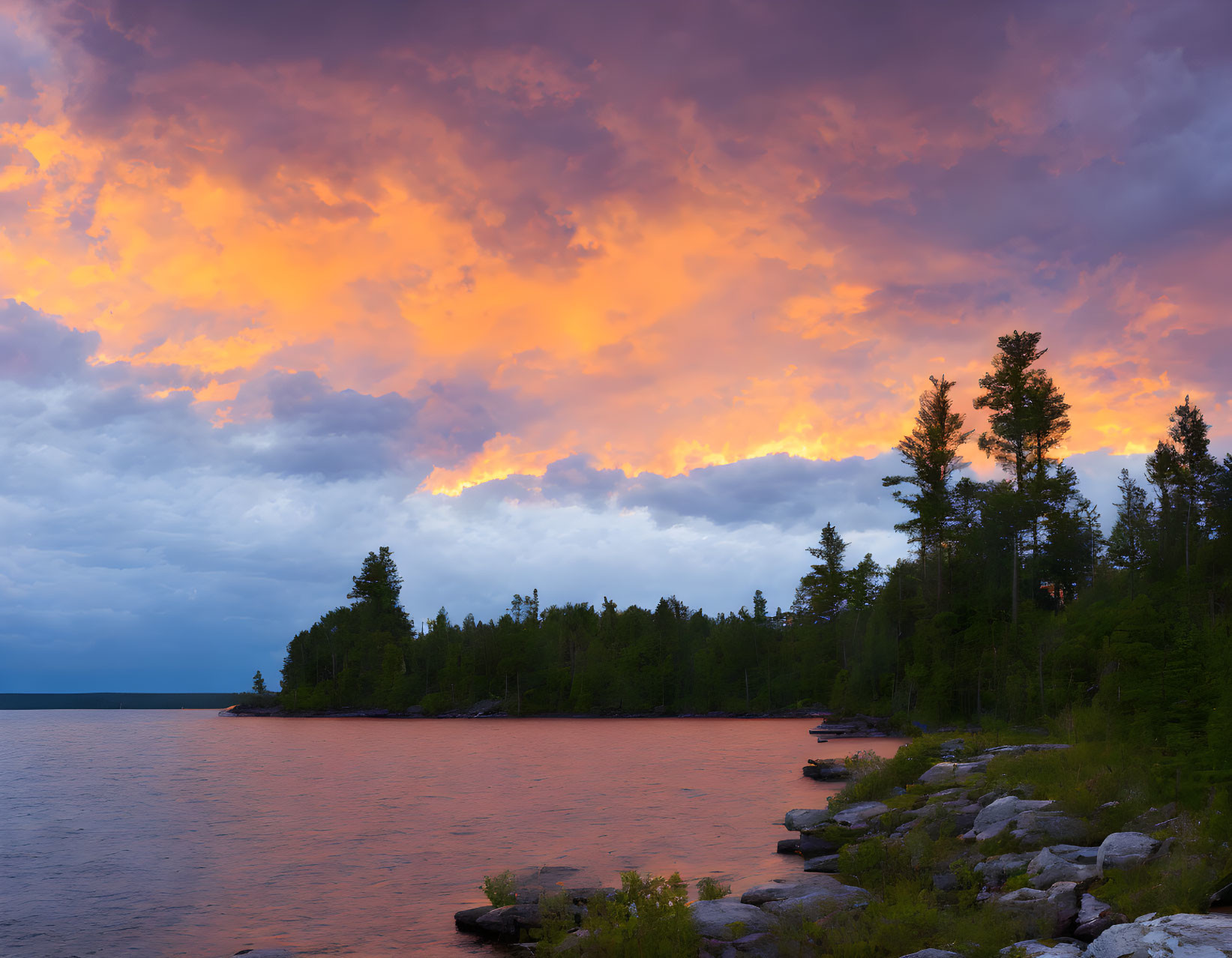 Fiery orange sunset over tranquil lake and forested shoreline