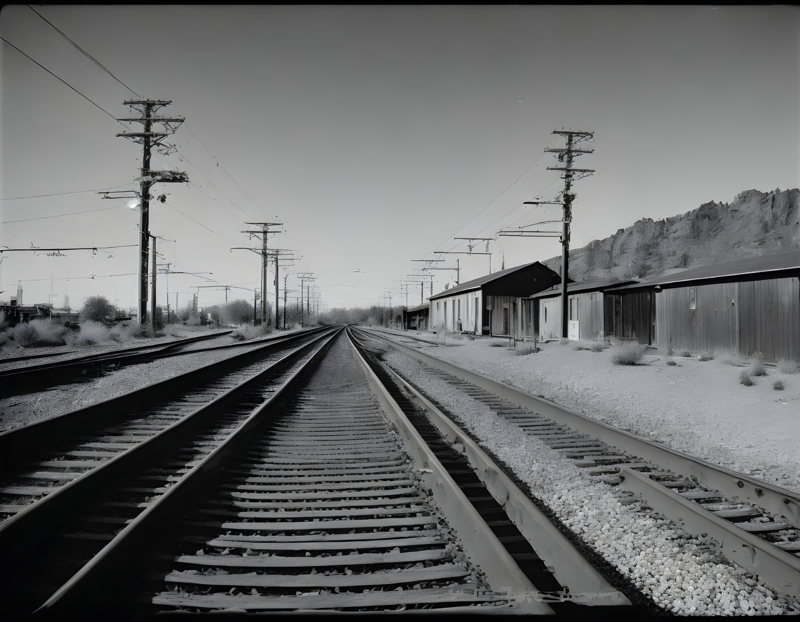 Monochrome image of railroad tracks, telephone poles, and buildings under clear sky