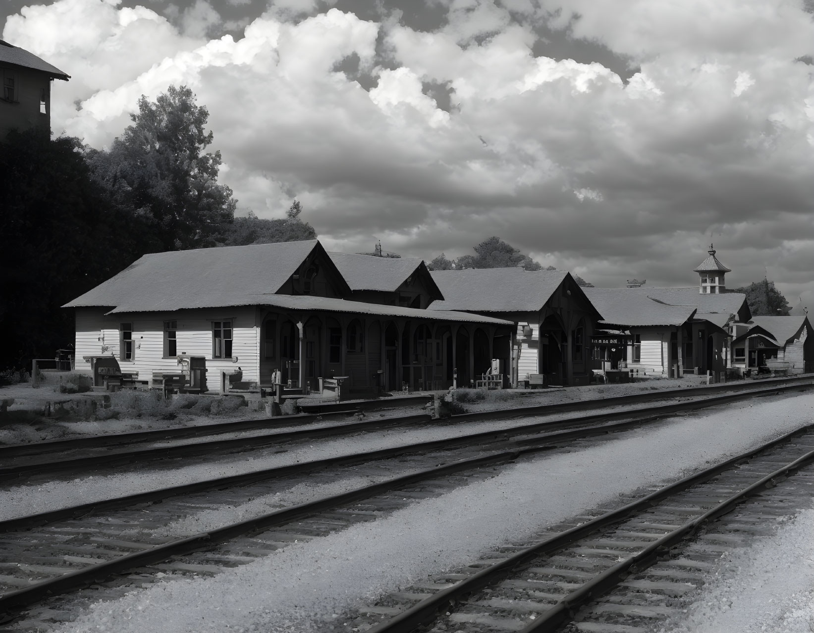 Deserted railway station with multiple tracks and vintage buildings under cloudy sky