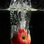 Ripe tomato splashing in water with bubbles and droplets on dark background