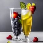 Fruit-filled glasses with honeycomb pattern, mint leaf, lemon slice, and strawberries on reflective surface