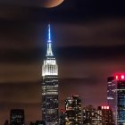 Night cityscape with illuminated skyscraper and surreal moon in starry sky