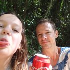 Two girls sharing Coca-Cola with realistic dinosaurs in lush setting.