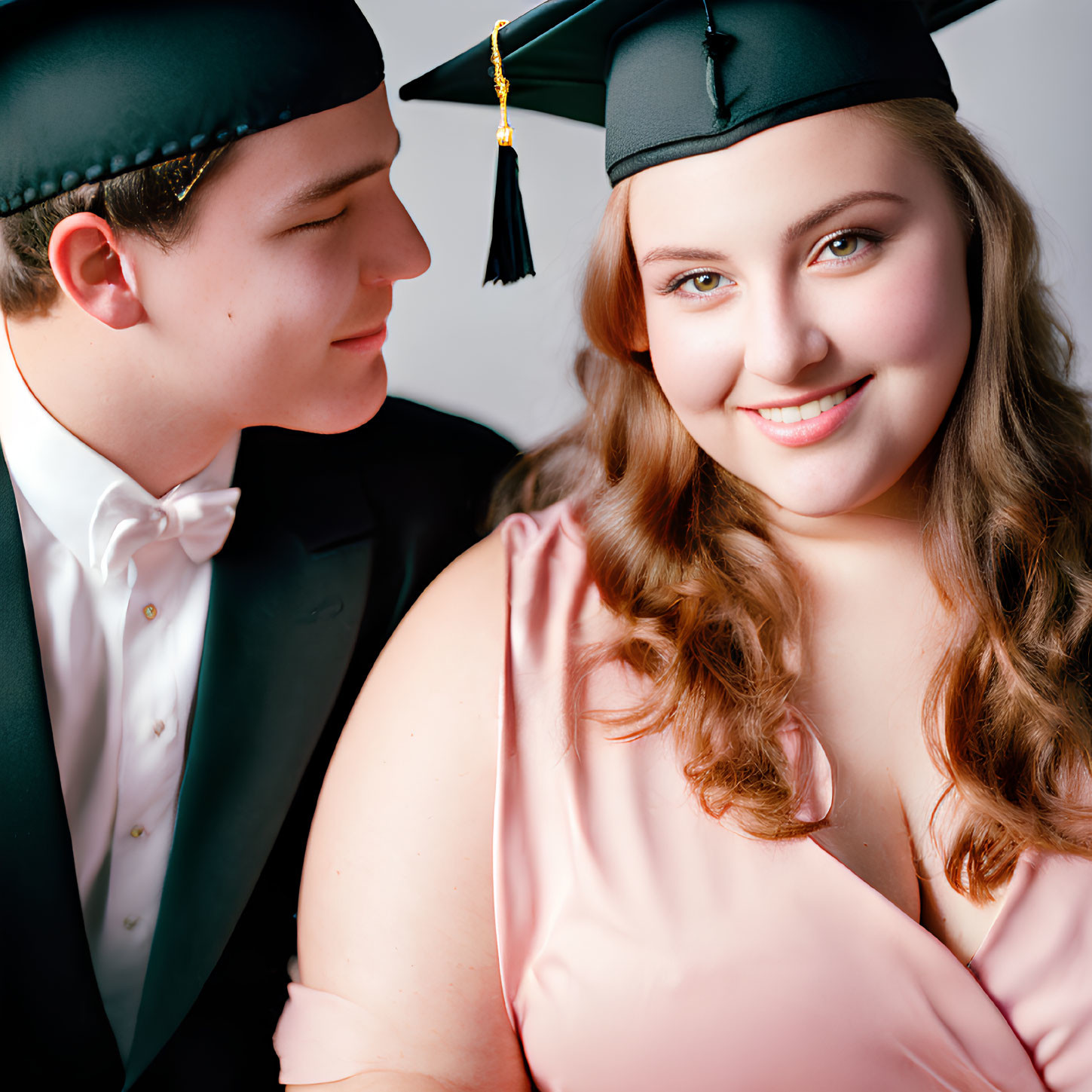 Formal young couple: woman in graduation cap, man in tuxedo, smiling closely