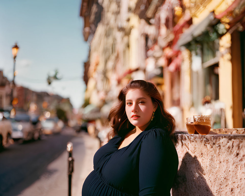 Woman in Blue Dress Leaning on Stone Ledge with Drink on Sunny City Street