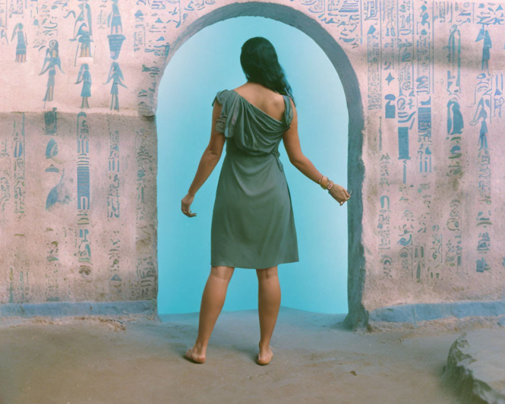 Barefoot person in grey dress by Egyptian hieroglyphic doorway