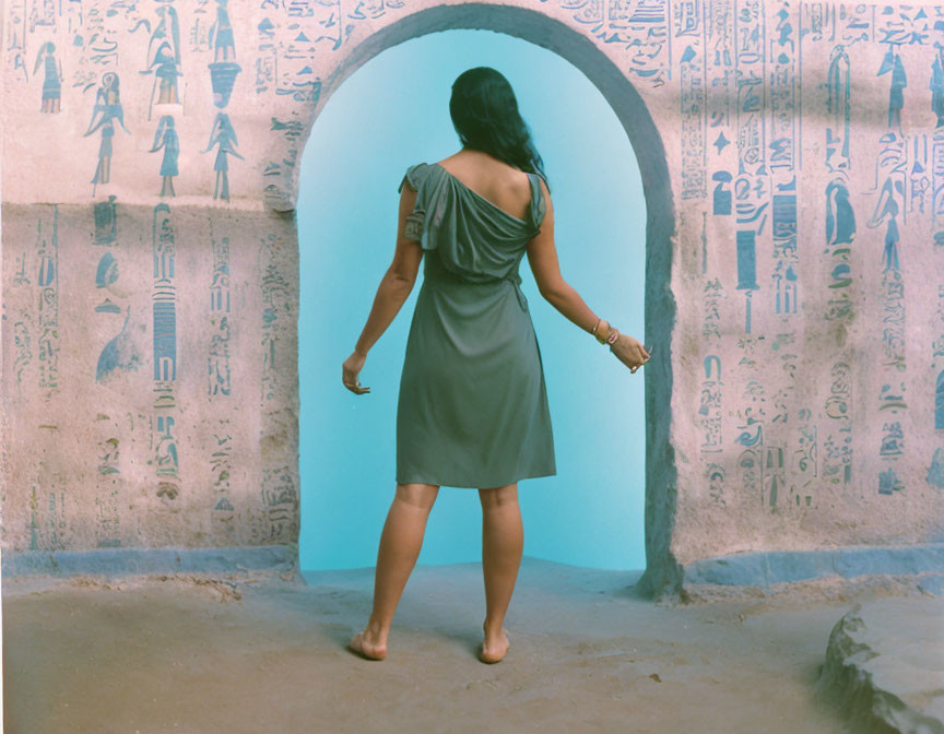 Barefoot person in grey dress by Egyptian hieroglyphic doorway