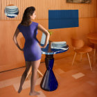 Woman in blue dress and white heels in orange room with round table and artwork.