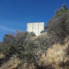 Stone castle on forested hill under clear sky with path to gates