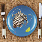 Cooked isopod with lime on blue plate, fork and knife on brown surface