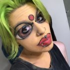 Abstract Picasso-style face paint with multiple eyes and lips, neon green hair