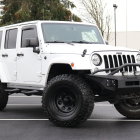 White Four-Door Jeep Wrangler on Gravel Road with Forest Background