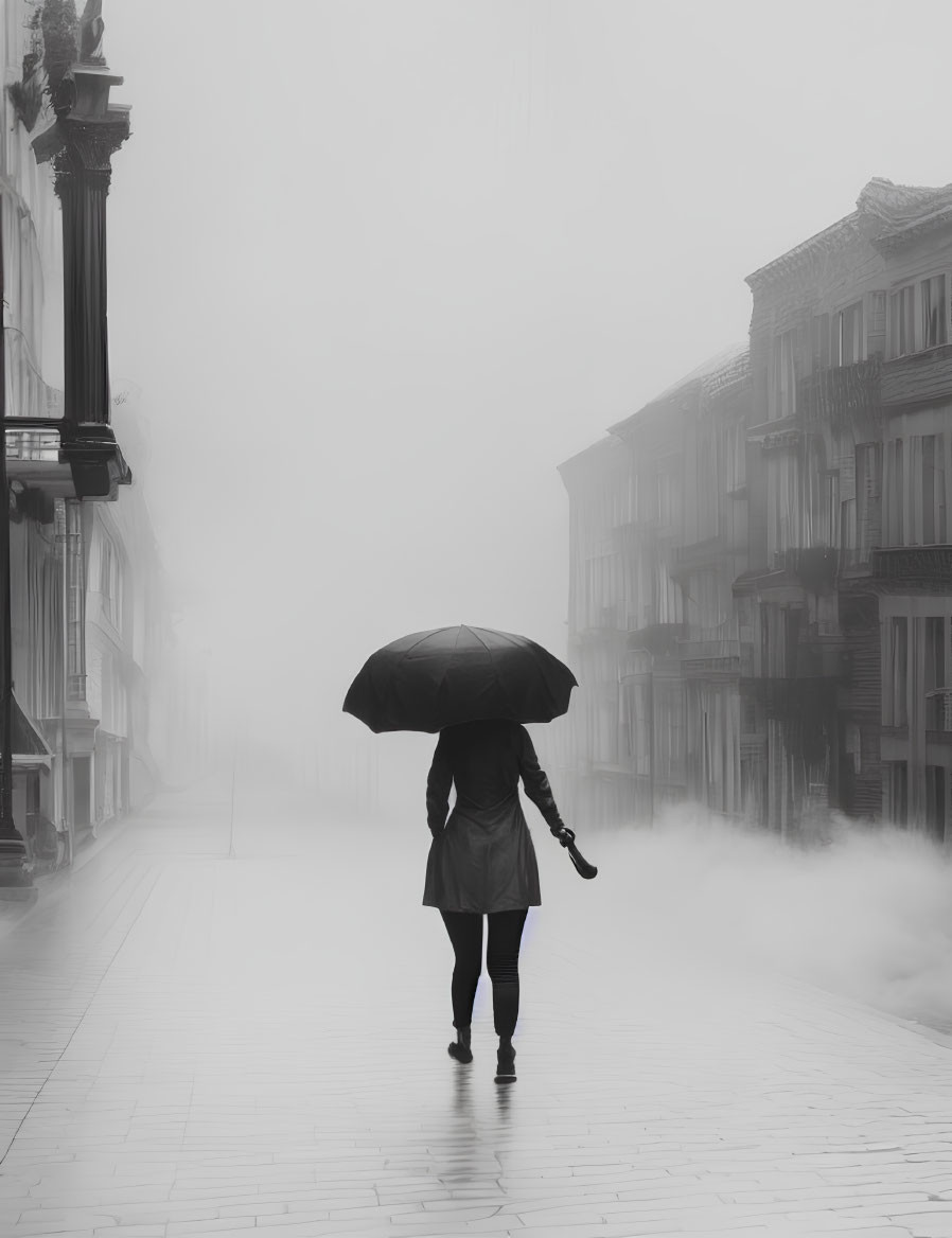 Person with umbrella walking on foggy street between buildings