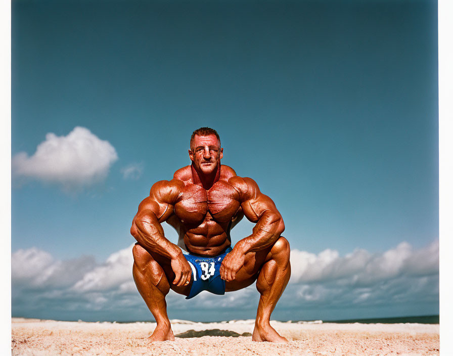 Muscular person crouching on sandy beach under blue sky