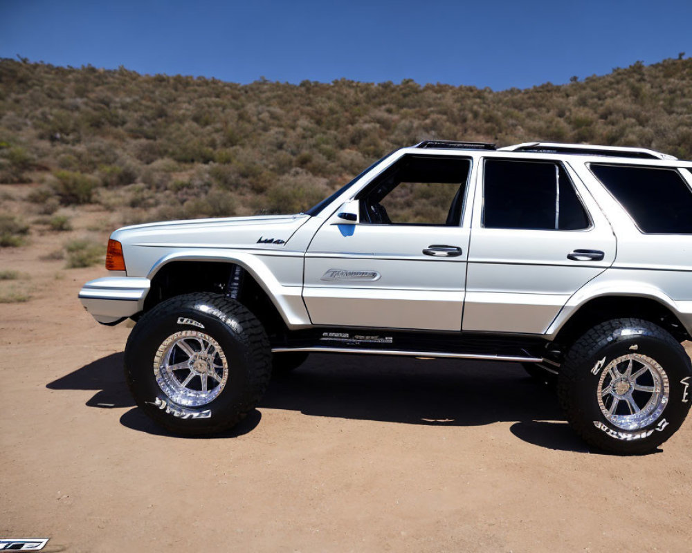 White Jeep Grand Cherokee with off-road tires on dirt terrain