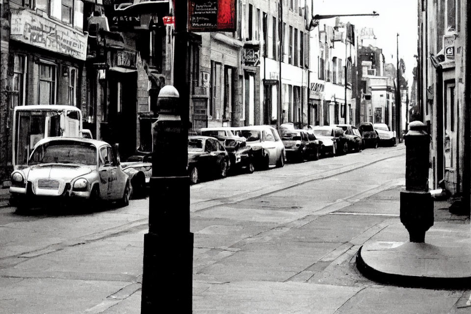 Vintage black and white photo of narrow street with parked cars and old shopfronts