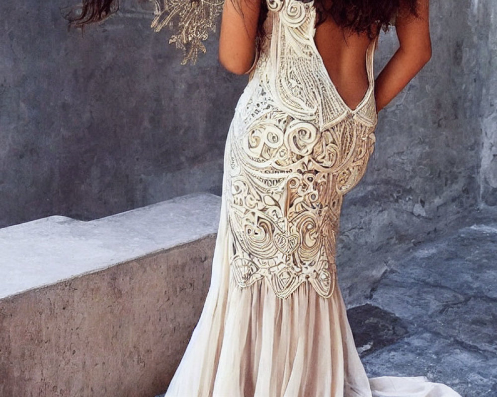 Intricate lace wedding dress with open back design on woman against grey wall