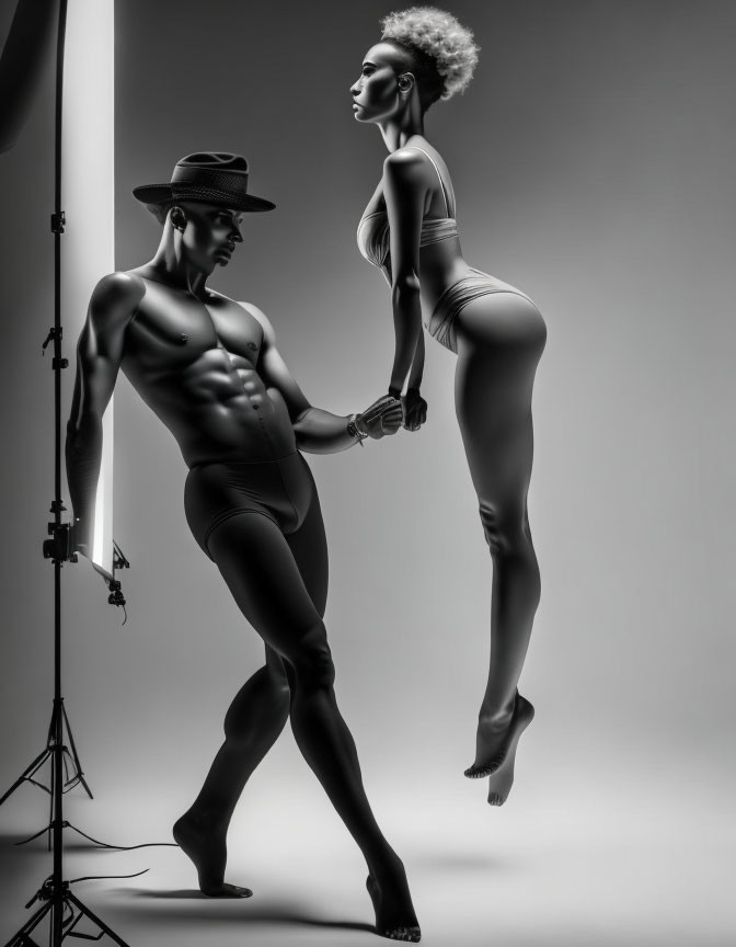 Monochrome studio photo: Fit male and female models pose with dramatic lighting, male in a hat,