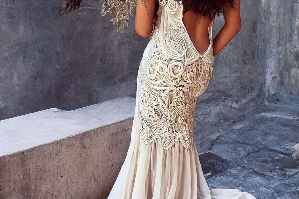 Intricate lace wedding dress with open back design on woman against grey wall