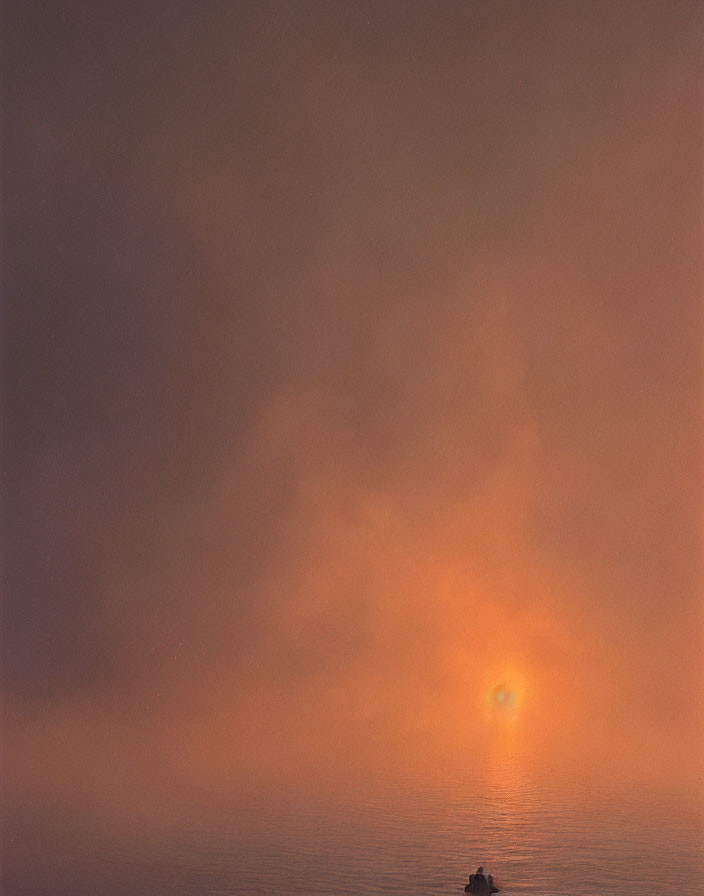 Solitary boat on calm sea under hazy sky with warm glow