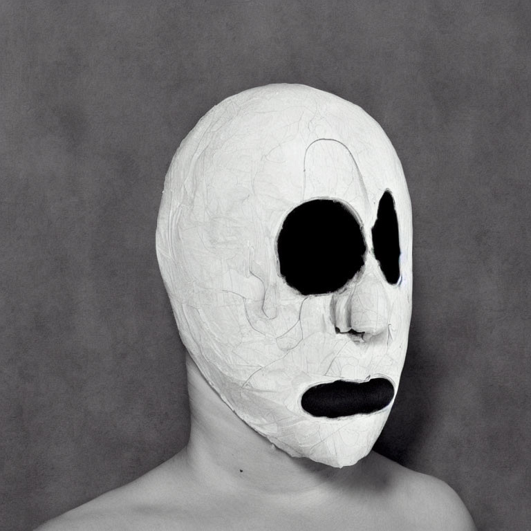 White Textured Mask with Asymmetric Black Eye Holes and Mouth Opening on Grey Background