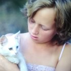 Young girl holding white cat with blue eyes on soft background