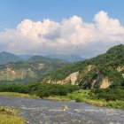 Tranquil river landscape with greenery, clouds, and buildings