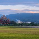 Orthodox-style churches in lush green field with layered mountain ridges at dusk