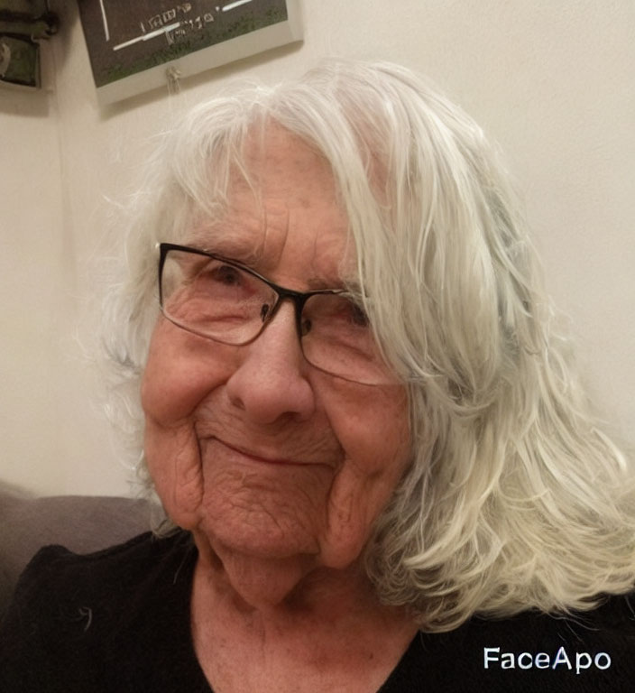 Elderly lady with glasses and white hair smiling indoors with watermark