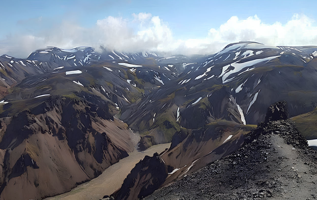 Panoramic rugged mountain landscape with snow patches under cloudy sky