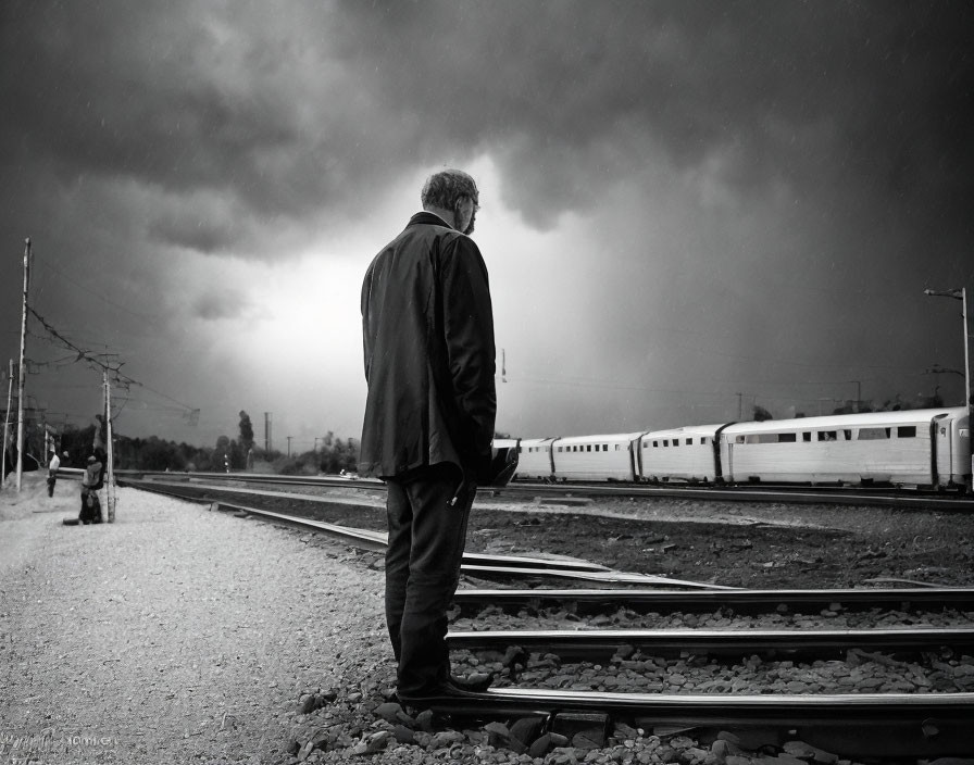 Elderly man on train tracks under dramatic cloudy sky