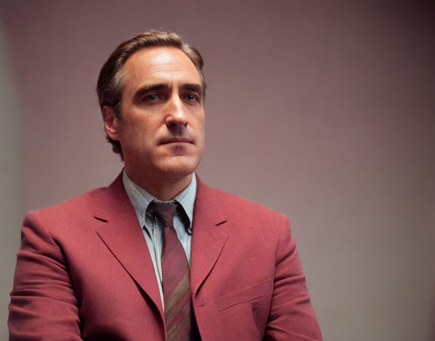 Man in suit with patterned tie and short hair gazes thoughtfully.