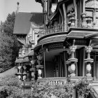 Victorian house with ornate woodwork, wraparound porch, flowers, and lush trees