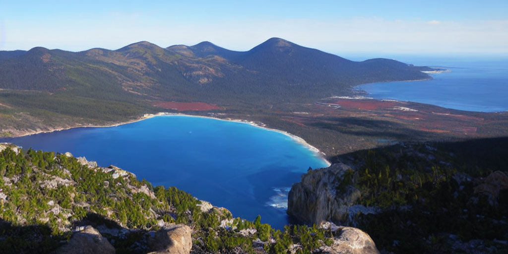 Serene blue lake with forested mountains and ocean view.