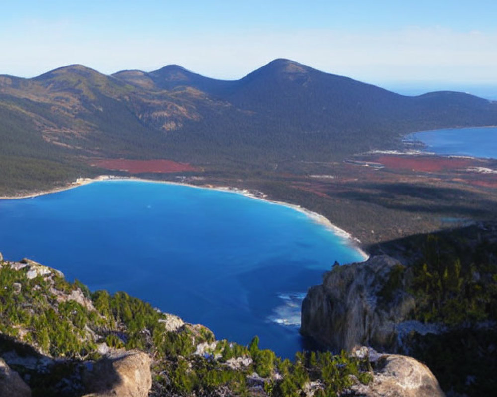 Serene blue lake with forested mountains and ocean view.