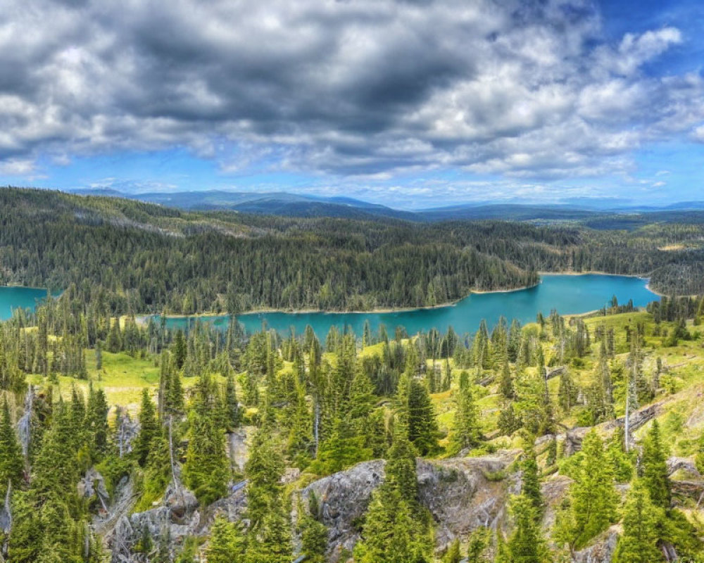 Scenic panoramic view of vibrant blue lake, green forests, and rocky terrain under dynamic sky