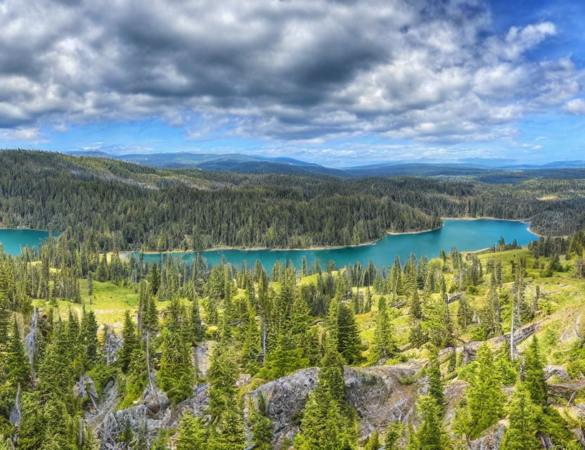 Scenic panoramic view of vibrant blue lake, green forests, and rocky terrain under dynamic sky