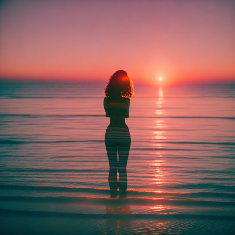 Woman on beach at sunset with sun's reflection and pink-orange sky