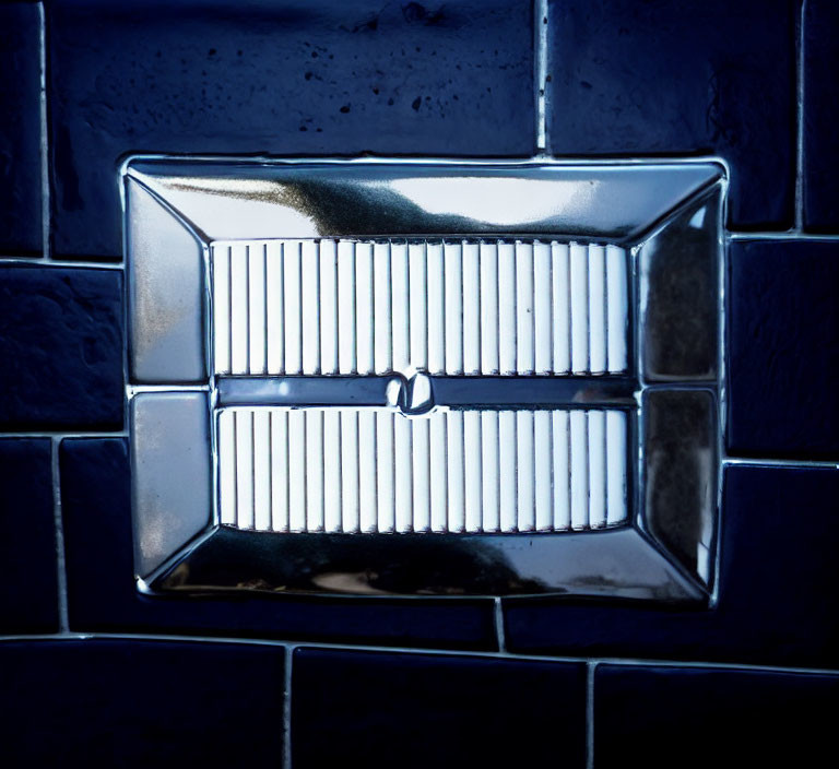 Silver Bathroom Vent Reflecting Light on Dark Tiled Wall