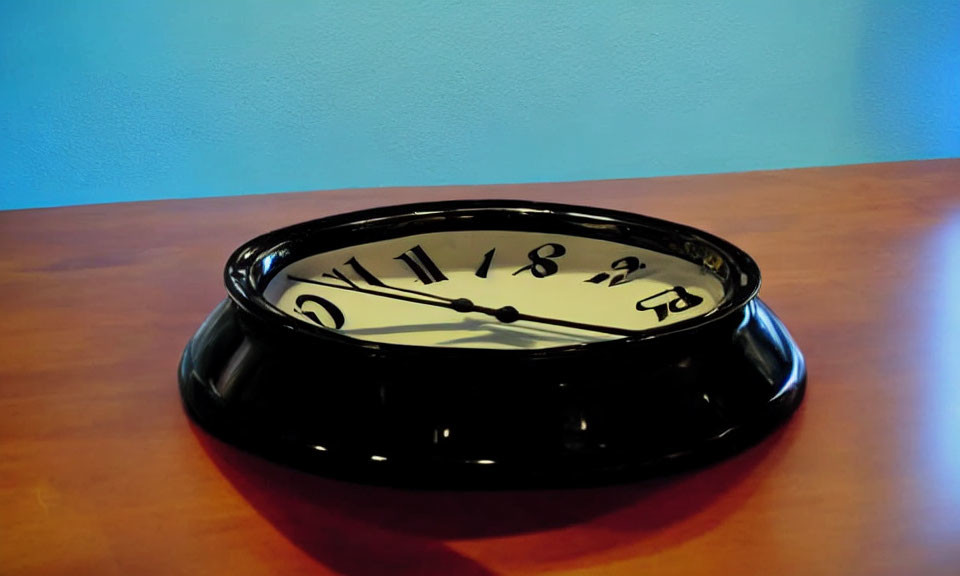 Distorted black wall clock with skewed face on wood surface against blue wall