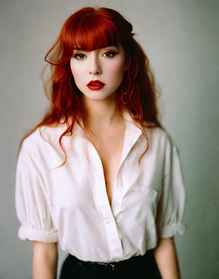 Red-haired woman with bangs in white blouse and red earrings gazes at camera.