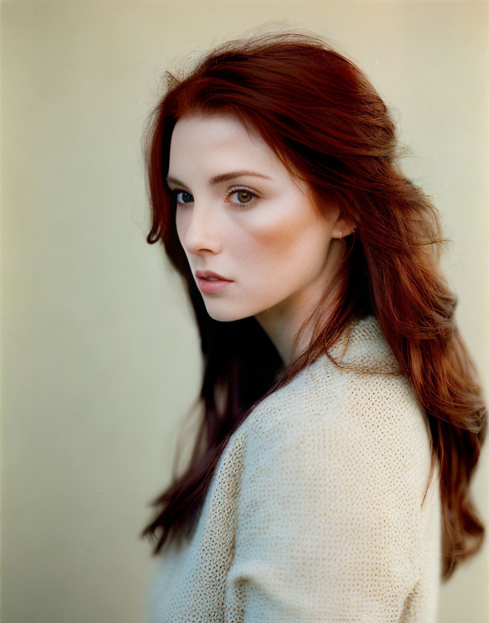 Long red hair woman with fair skin looking over shoulder on beige background