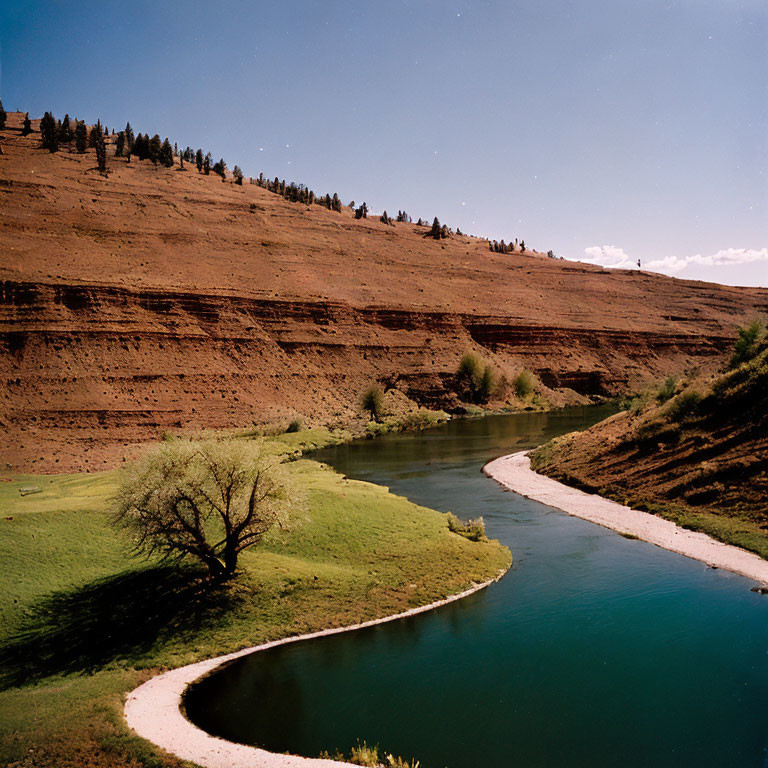 Tranquil river winding through lush green landscape with tree, red-rock cliffs, and blue sky