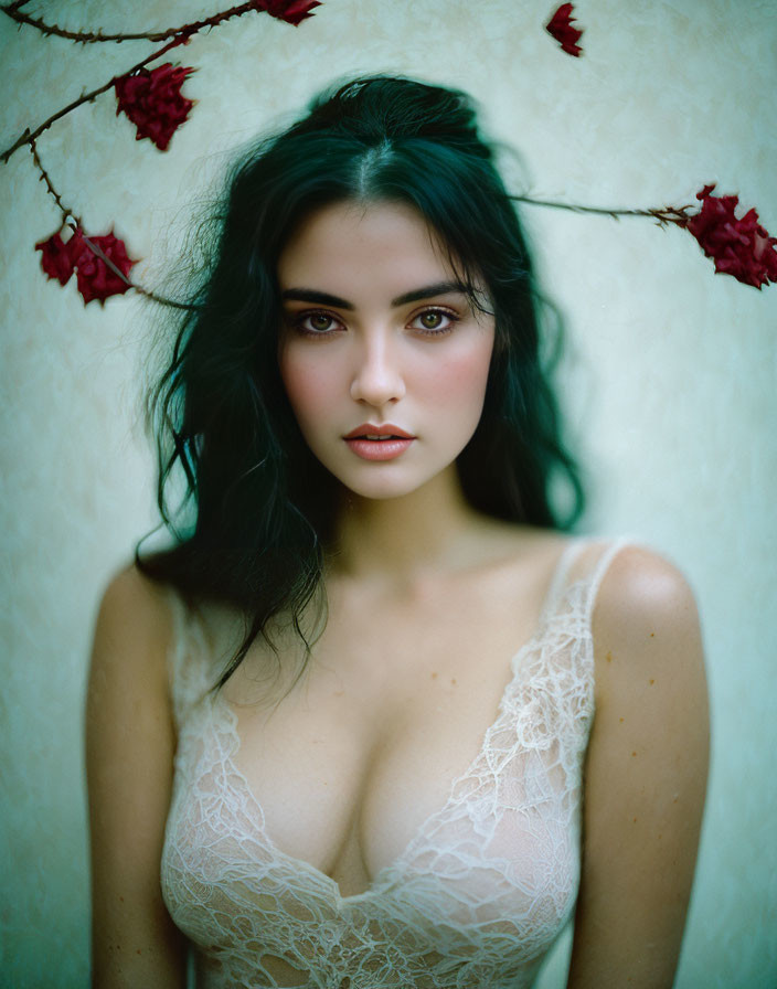 Dark-haired woman with striking eyes surrounded by red flowers in white lace attire.