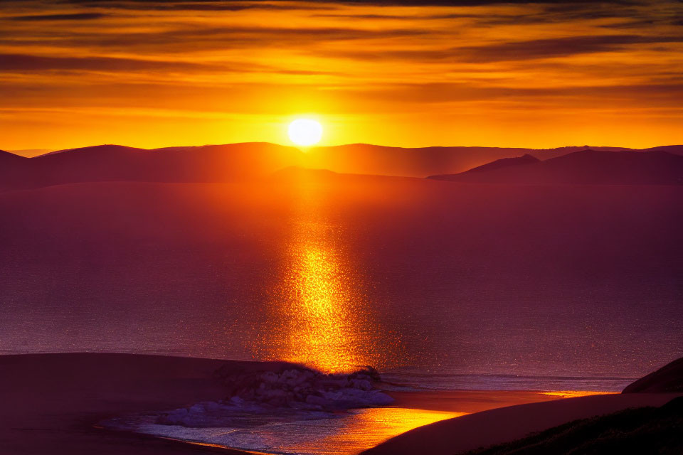 Scenic sunset over tranquil sea with golden reflection, silhouetted mountains, and gentle waves